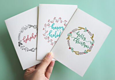 Cropped Hand Holding Christmas Cards With Text Over Turquoise Background